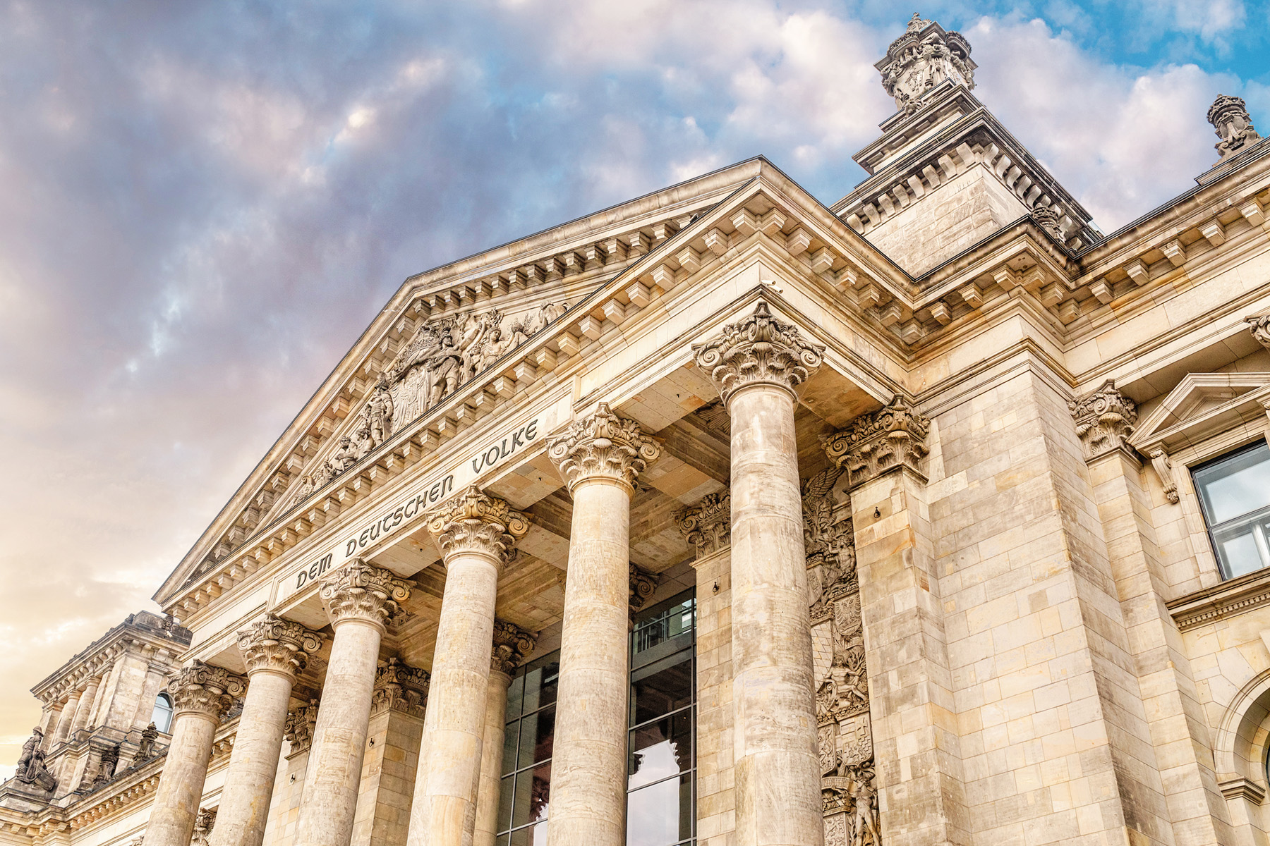 Das Bild zeigt die neoklassizistische Fassade des Reichstagsgebäudes in Berlin mit hohen Säulen und detaillierten Steinmetzarbeiten.